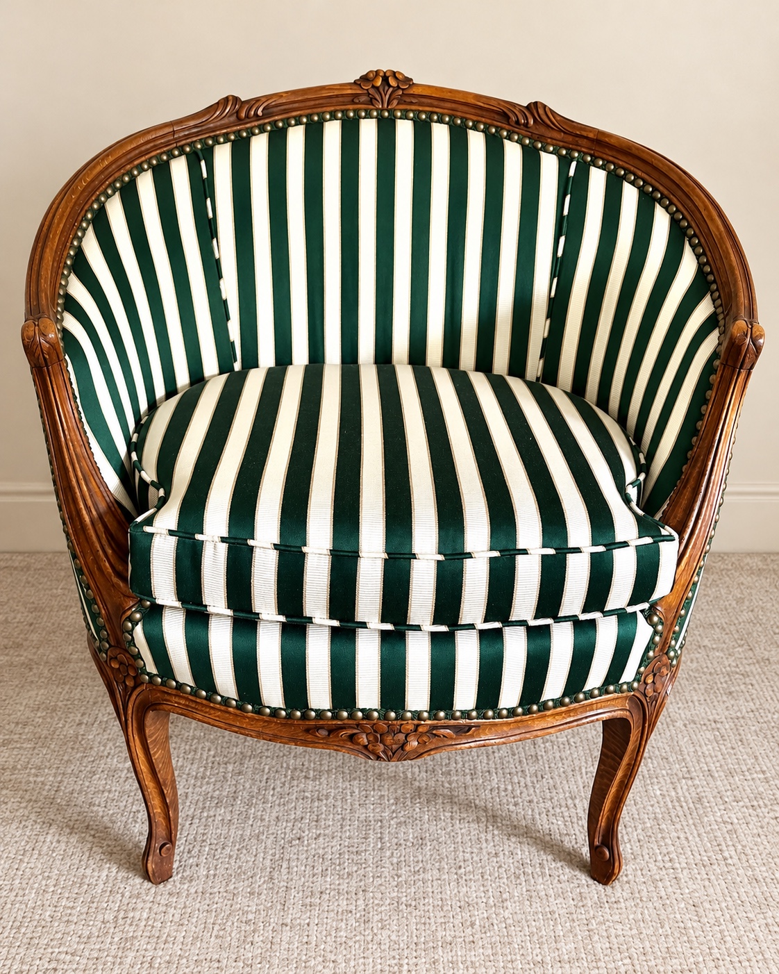 Green-and-cream striped barrel chair with carved timber frame and nailhead trim, shown with wider framing against a refined cream backdrop. Photo edited for presentation.